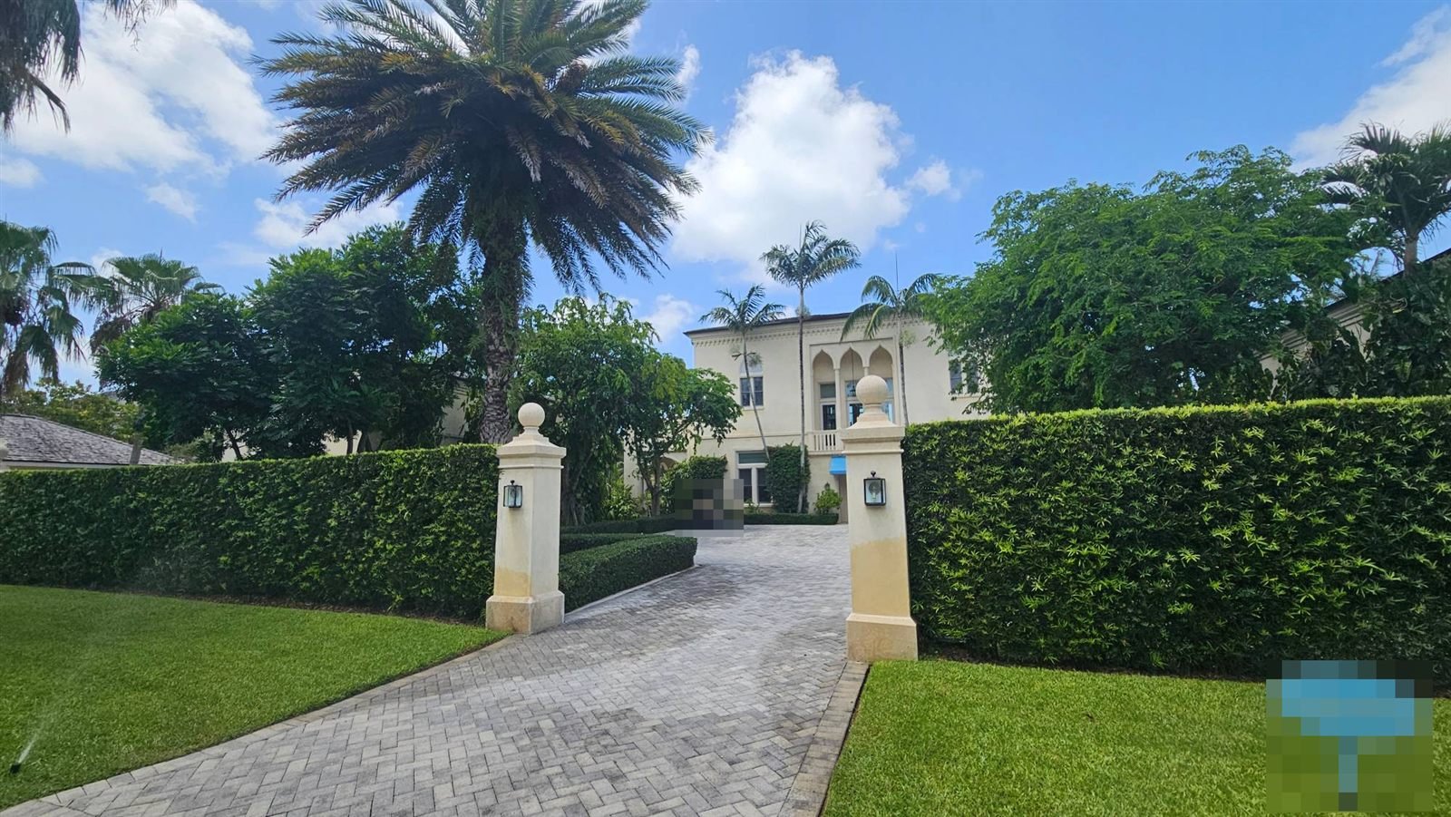 Gated villa with a paved driveway and tall hedges